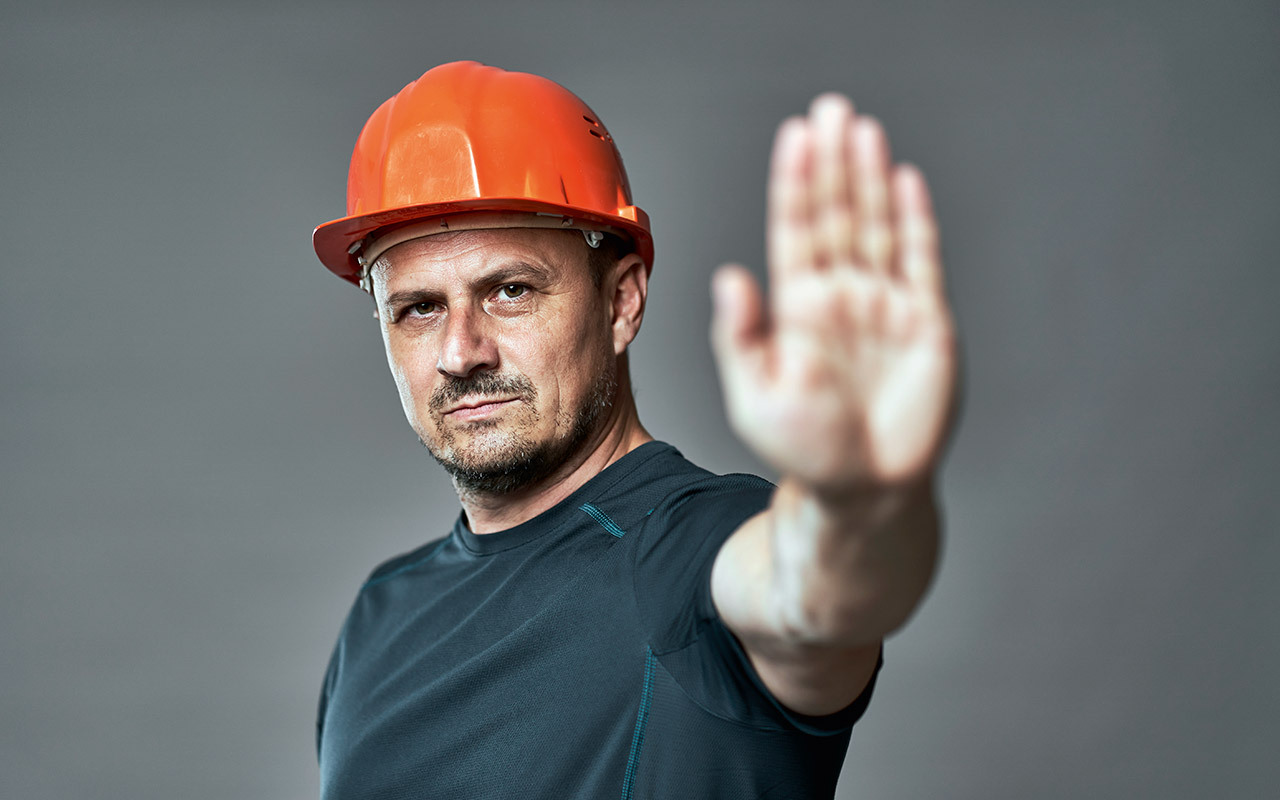 Man with helmet stretches palm toward camera and shows stop